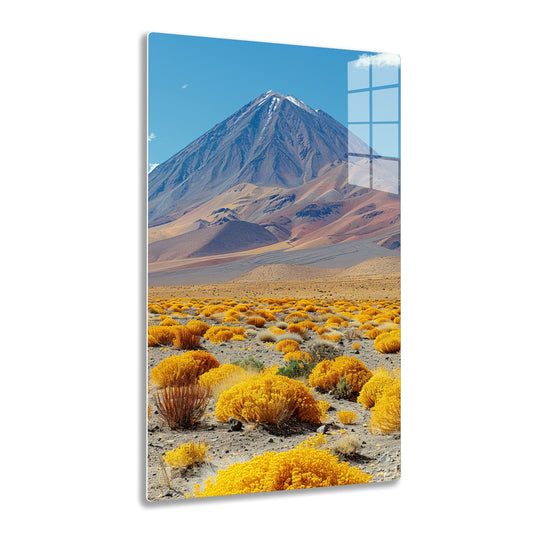 A majestic snow-capped mountain rises against a vivid blue sky, surrounded by a vast landscape of undulating hills and shrubs with vibrant yellow and rusty hues in the foreground.
