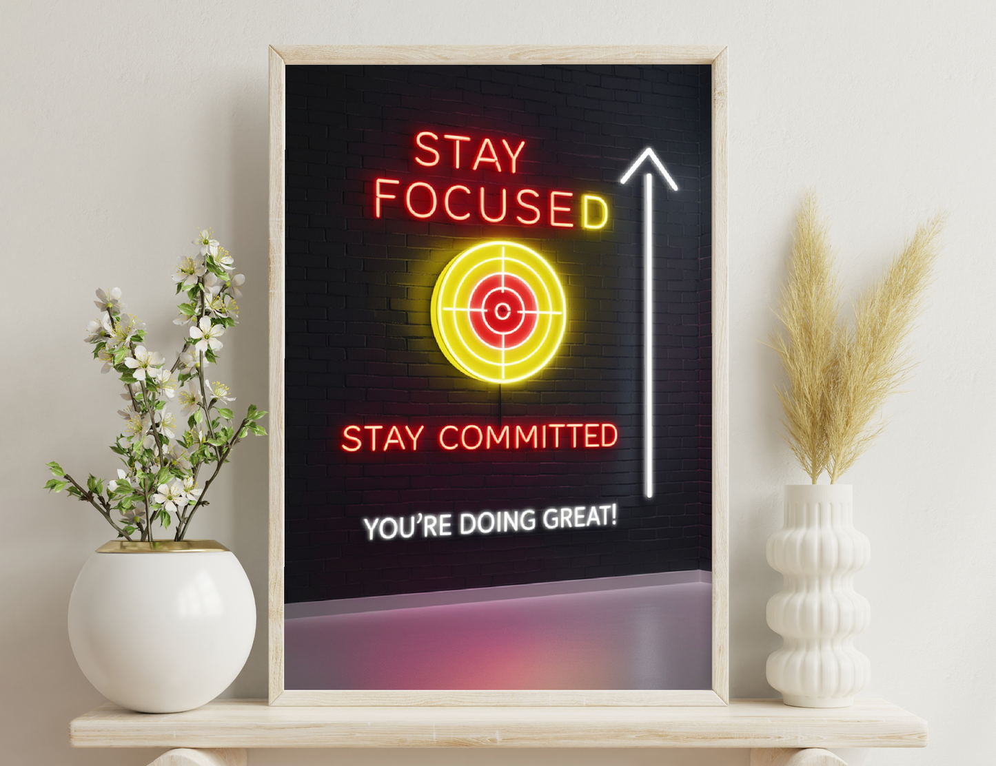 A neon sign on a brick wall displays motivational messages: "Stay Focused" with a target icon, "Stay Committed," an upward arrow, and "You're Doing Great!"
