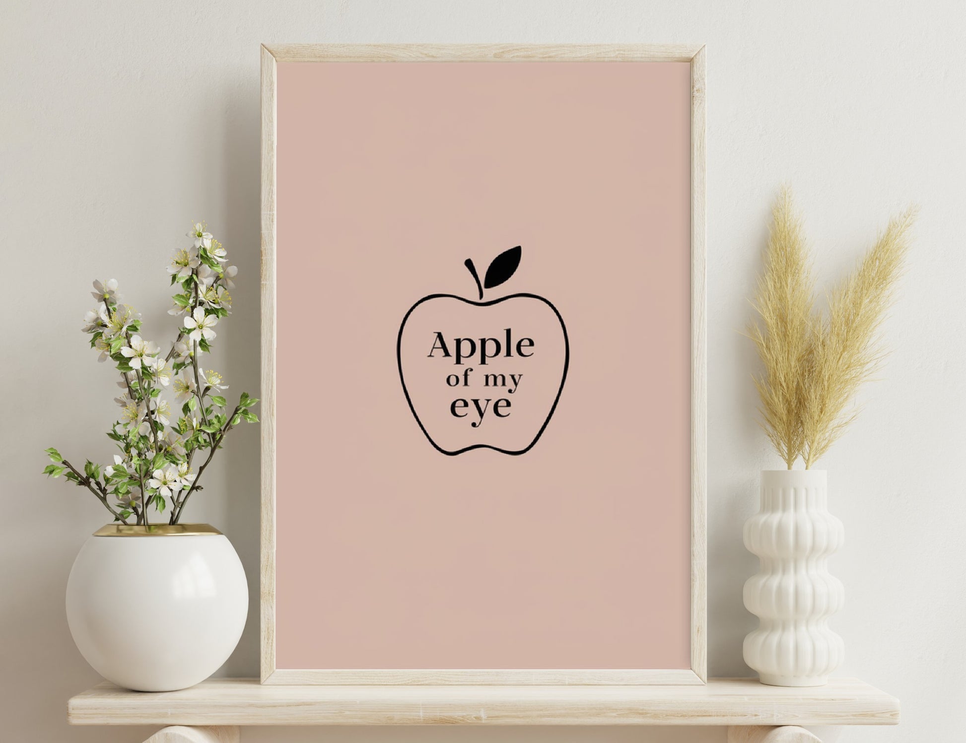 Apple illustration with the text "Apple of my eye" written inside, depicted on a light pink background.
