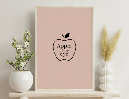 Apple illustration with the text "Apple of my eye" written inside, depicted on a light pink background.
