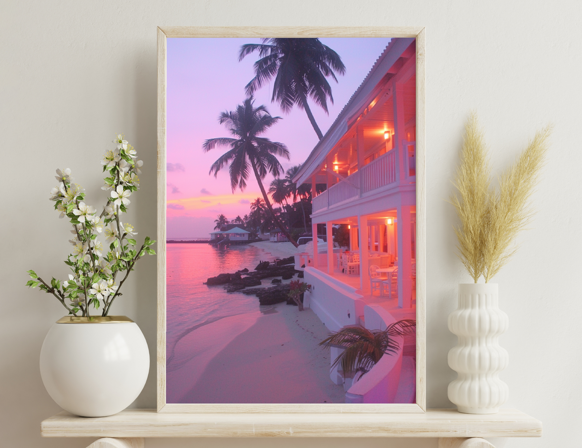 A beachfront resort with palm trees and a warm pink sunset sky, featuring a long building with red lights along the waterfront and a small boat dock in the distance.
