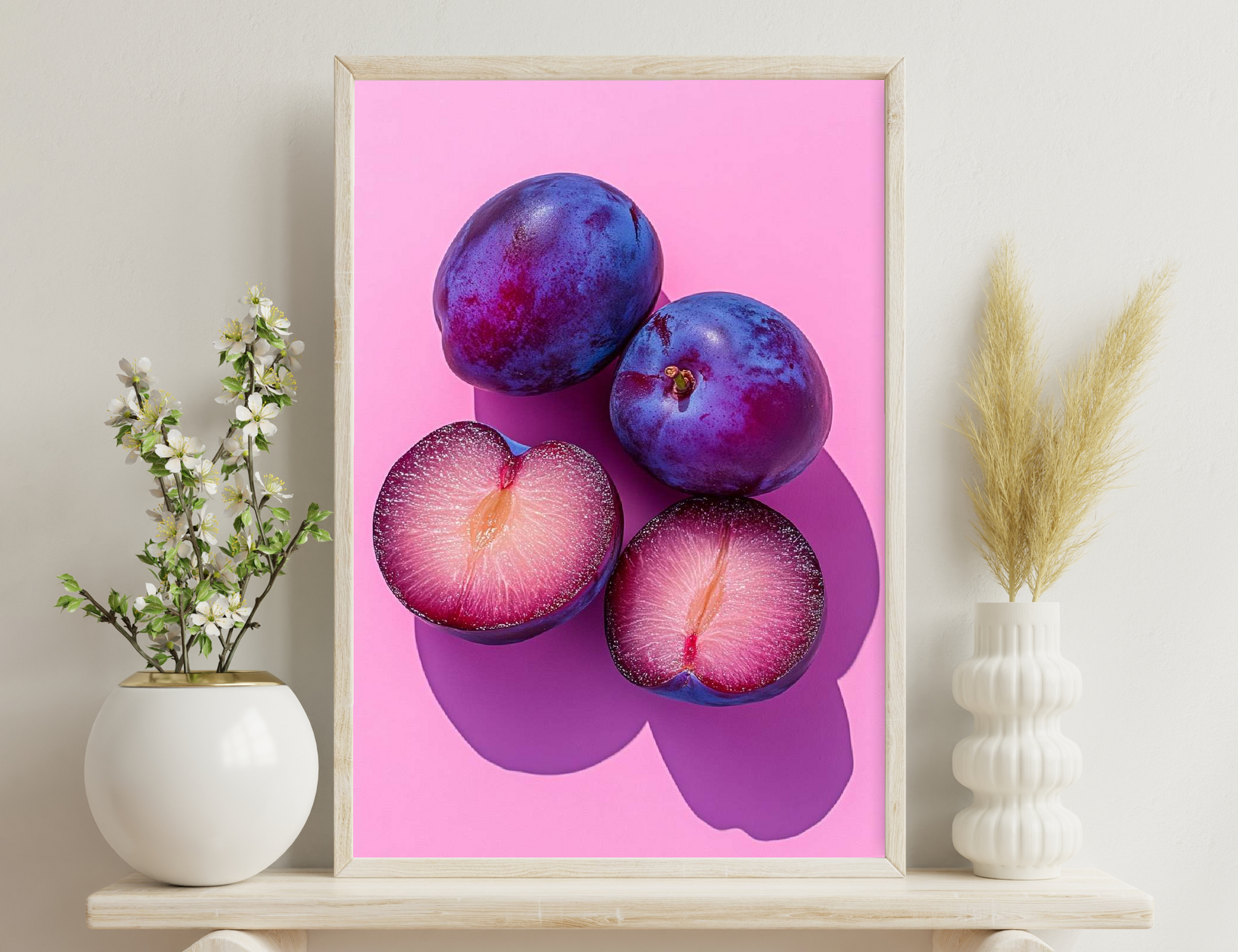 Two whole purple plums and two halved plums with bright pink and crimson interiors against a vivid pink background
