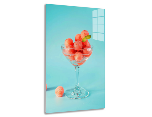 A glass bowl filled with ripe, juicy watermelon balls garnished with a mint leaf, against a blue background.
