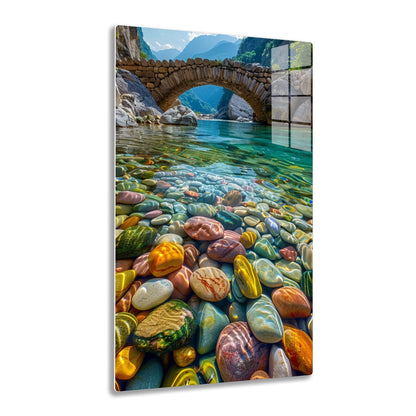 A beautiful stone bridge arches over a crystal-clear river running through a mountainous gorge, with the riverbed covered in smooth, colorful pebbles that create a mesmerizing pattern of vibrant colors and natural textures.
