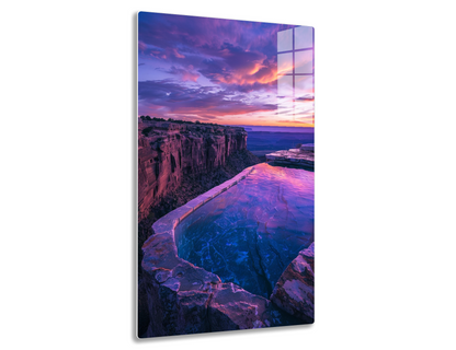 Stunning sunset over rocky coastline with vibrant purple and orange clouds reflecting in a curved tide pool along the clifftop path.
