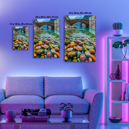 A beautiful stone bridge arches over a crystal-clear river running through a mountainous gorge, with the riverbed covered in smooth, colorful pebbles that create a mesmerizing pattern of vibrant colors and natural textures.
