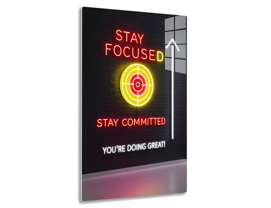 A neon sign on a brick wall displays motivational messages: "Stay Focused" with a target icon, "Stay Committed," an upward arrow, and "You're Doing Great!"
