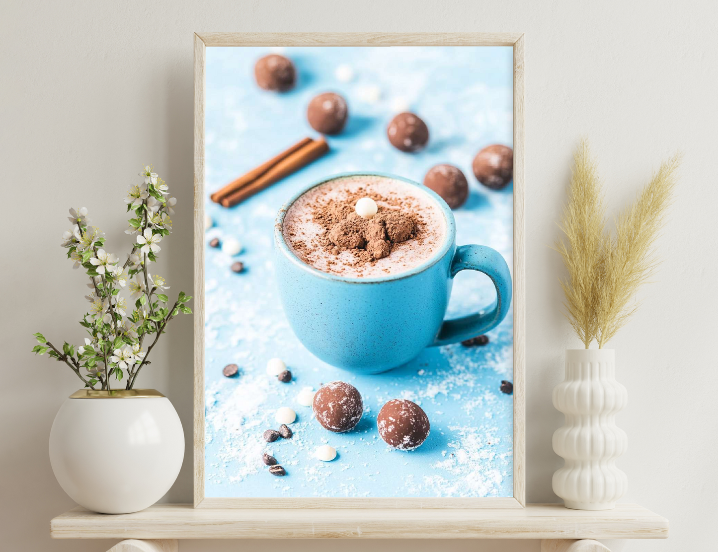 A blue mug filled with hot chocolate topped with whipped cream and cocoa powder, surrounded by cinnamon sticks, chocolate truffles, and scattered cocoa beans on a blue background.
