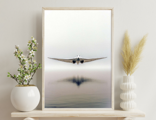 A low-flying military jet with swept wings skims across a misty lake surface, its reflection mirrored perfectly in the still water below.
