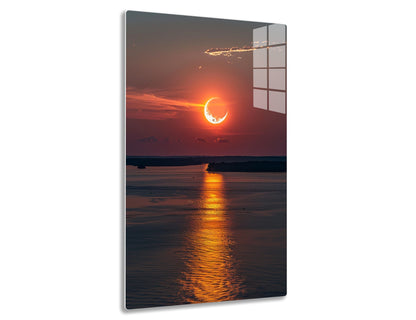 A crescent sun setting over a reflective lake, casting a fiery orange glow and sun trail on the rippling water against a cloudy sky.
