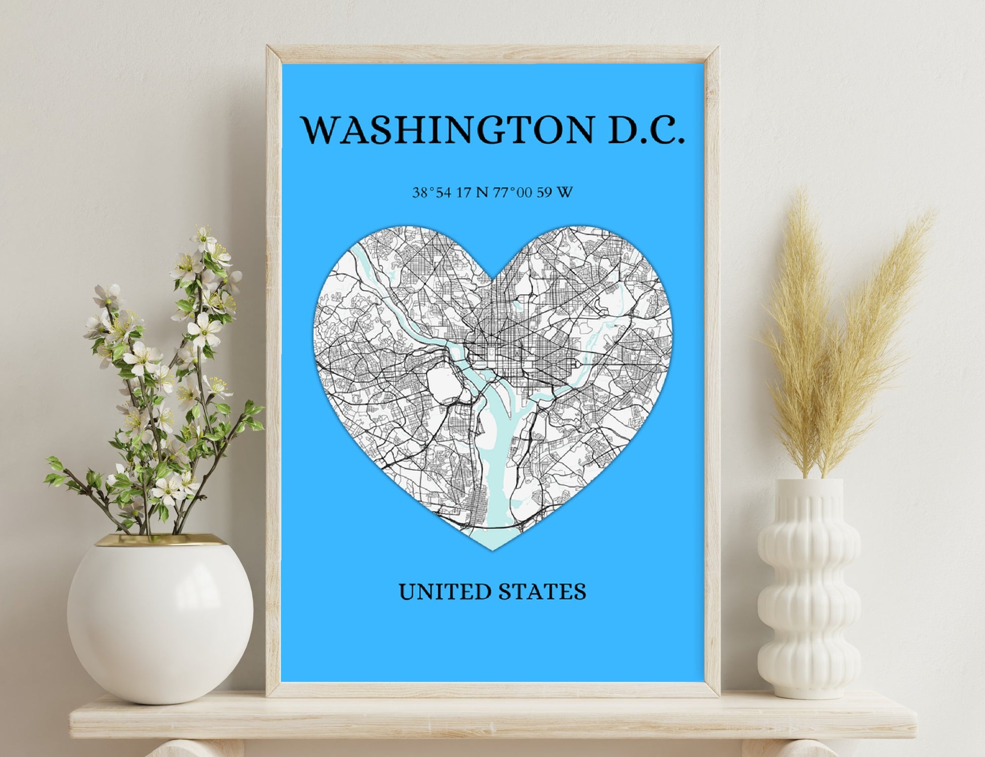 A map of Washington D.C. in the shape of a heart, showing the district's roads and waterways against a blue background, along with its geographic coordinates and the text "United States" below.
